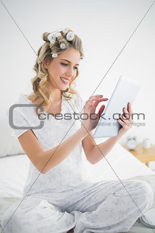 Happy blonde wearing hair curlers using tablet