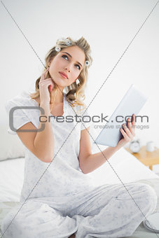 Thoughtful cute blonde wearing hair curlers using tablet