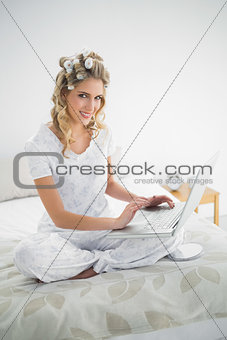 Cheerful cute blonde wearing hair curlers using laptop