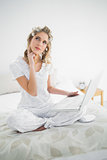 Pensive cute blonde wearing hair curlers using laptop