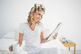 Smiling cute blonde wearing hair curlers reading newspaper