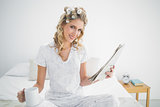 Smiling cute blonde wearing hair curlers holding newspaper
