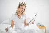 Peaceful cute blonde wearing hair curlers holding newspaper