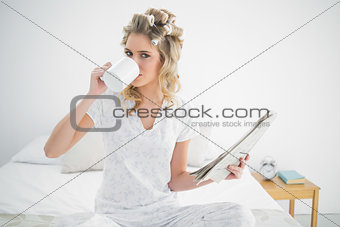 Peaceful cute blonde wearing hair curlers drinking coffee