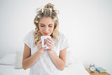 Peaceful cute blonde wearing hair curlers smelling coffee
