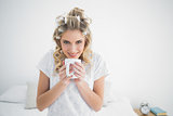 Smiling cute blonde wearing hair curlers smelling coffee