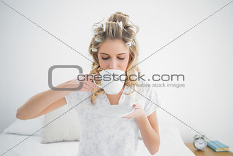 Peaceful blonde wearing hair curlers drinking coffee