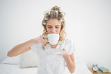 Relaxed pretty blonde wearing hair curlers drinking coffee