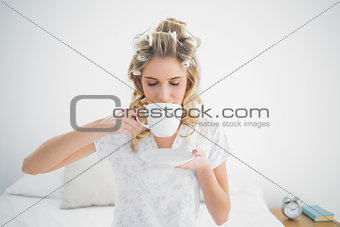 Relaxed pretty blonde wearing hair curlers drinking coffee
