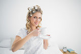 Relaxed pretty blonde wearing hair curlers holding coffee