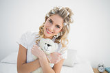 Smiling pretty blonde wearing hair curlers holding teddy bear