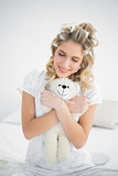 Peaceful pretty blonde wearing hair curlers holding teddy bear