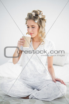Peaceful pretty blonde wearing hair curlers smelling coffee