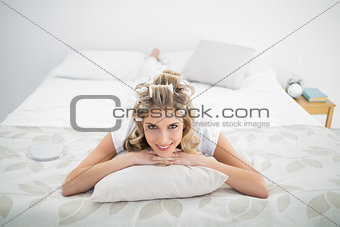Peaceful pretty blonde wearing hair curlers lying on bed