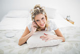 Smiling blonde wearing hair curlers on the phone