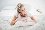 Cheerful blonde wearing hair curlers on the phone