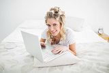 Cheerful blonde wearing hair curlers using laptop