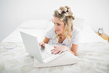 Relaxed pretty blonde wearing hair curlers using laptop