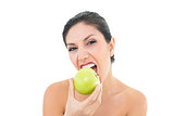 Happy brunette eating a green apple and looking at camera