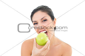 Happy brunette eating a green apple and looking at camera