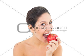 Happy brunette eating a red apple and looking at camera