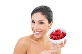Pretty brunette holding a bowl of fresh strawberries and smiling at camera