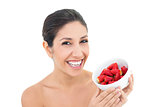 Attractive brunette holding a bowl of fresh strawberries and smiling at camera
