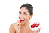 Attractive brunette holding a bowl of fresh strawberries and eating one