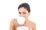 Pretty brunette holding a cup and saucer and taking a sip while winking