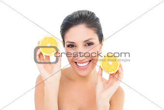 Happy brunette holding two orange halves and smiling at camera