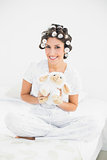 Brunette in hair rollers holding sheep teddy smiling at camera
