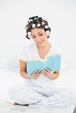 Happy brunette in hair rollers reading a book on bed