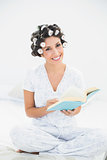 Smiling brunette in hair rollers reading a book on bed