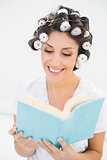 Cheerful brunette in hair rollers reading a book on bed