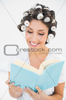 Cheerful brunette in hair rollers reading a book on bed