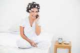 Happy brunette in hair rollers on the phone on bed