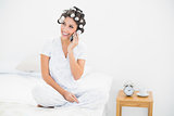 Smiling brunette in hair rollers on the phone on bed