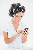 Pretty brunette in hair rollers using smartphone on bed