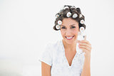 Pretty brunette in hair rollers holding glass of water smiling at camera
