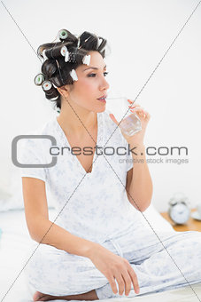 Pretty brunette in hair rollers drinking glass of water