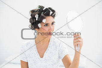 Happy brunette in hair rollers holding hand mirror