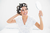 Happy brunette in hair rollers looking in hand mirror