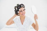 Smiling brunette in hair rollers holding hand mirror