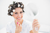 Happy brunette in hair rollers holding hand mirror and lip gloss