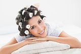 Pretty brunette in hair rollers lying on her bed smiling at camera