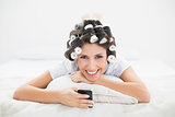 Happy brunette in hair rollers lying on her bed sending a text