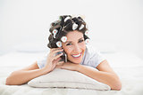 Smiling brunette in hair rollers lying on her bed making a phone call