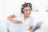 Smiling brunette in hair rollers lying on her bed using her tablet to shop online