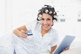 Smiling brunette in hair curlers lying on her bed using her tablet to shop online