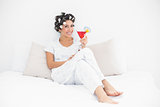 Smiling brunette in hair curlers sitting on her bed holding a cocktail
